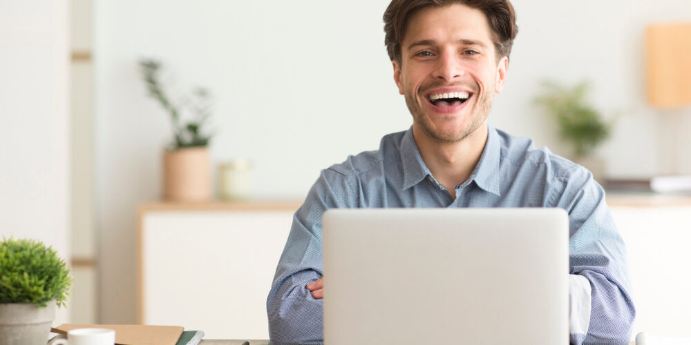 Man,Sitting,At,Laptop,And,Laughing,Looking,At,Camera,Indoor.