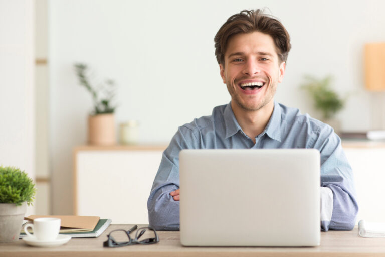 Man,Sitting,At,Laptop,And,Laughing,Looking,At,Camera,Indoor.